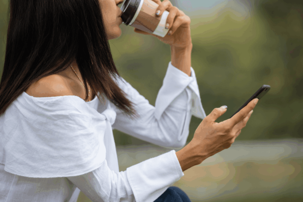 Mulher tomando café e mexendo em um iPhone da Casas Bahia