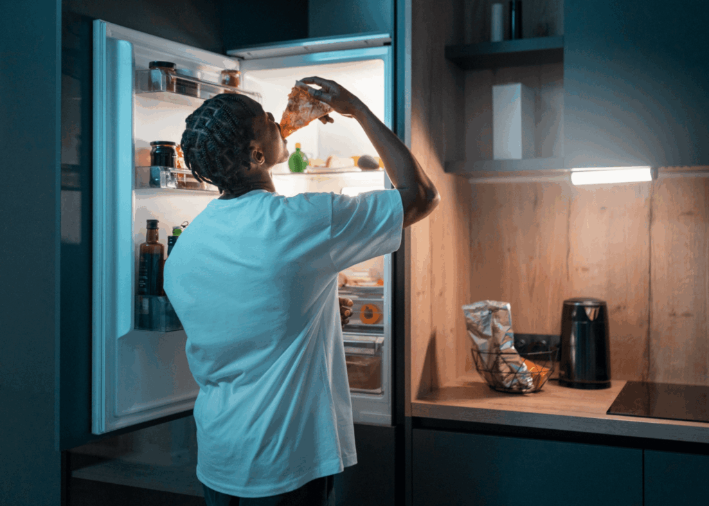 Homem comendo em frente à uma geladeira da Casas Bahia